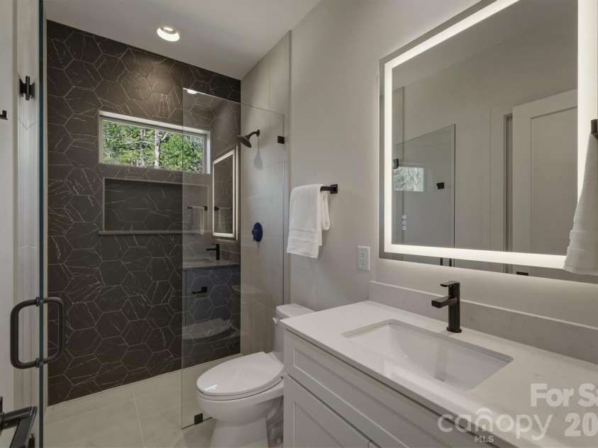 173 Waters Edge Drive, Nebo, NC 28761.  MLS# CAR4364596, YatesRealty ID 20742. Next, this bathroom can be accessed from the hall or from Bedroom Suite #2. There is a custom tiled zero entry shower with its custom glass door, a quartz counter top for the vanity and a great lighted mirror.
