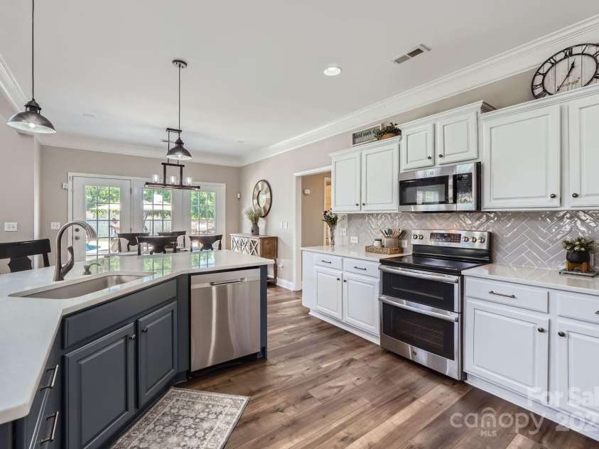 113 Dairy Farm Road, Mooresville, NC 28115.  MLS# CAR4262731, YatesRealty ID 20820. Crisp white cabinetry is complemented by a soft herringbone tile backsplash, quartz countertops, and a striking blue island that adds a pop of color and extra prep space.