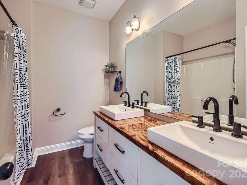 113 Dairy Farm Road, Mooresville, NC 28115.  MLS# CAR4262731, YatesRealty ID 20820. This stylish second-floor bathroom makes a bold statement with its custom wood countertop, dual vessel sinks, and matte black fixtures. A full-width mirror enhances the sense of space and light, while the sleek vanit