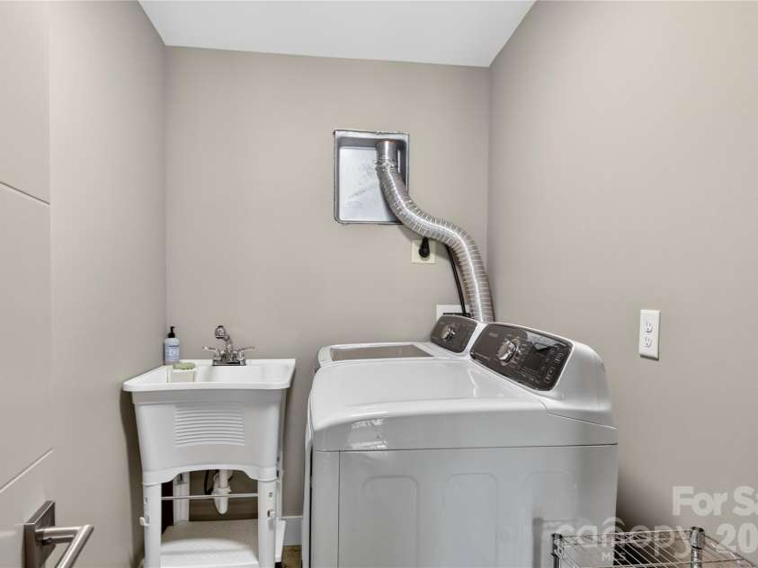 141 Round Top Circle, Mills River, NC 28759.  MLS# CAR4379751, YatesRealty ID 21136. Convenient lower-level laundry room offering practical space and easy accessibility, complete with washer, dryer, and utility sink for added functionality.