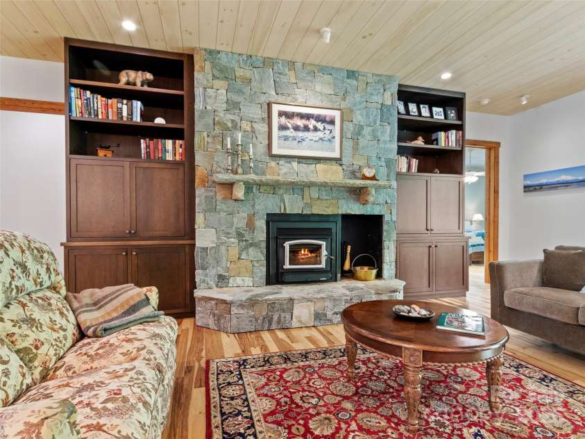 971 Banks Creek Road, Burnsville, NC 28714.  MLS# CAR4270100, YatesRealty ID 21780. Features a wood-burning Buck stove set against stunning stonework, complete with a handcrafted stone mantel and custom built-ins.