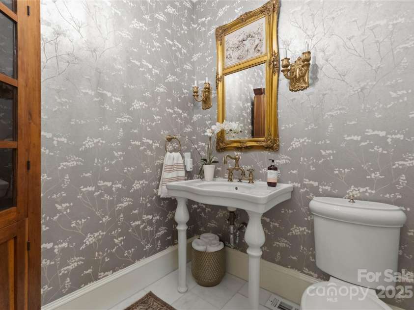 215 Main Street, Belmont, NC 28012.  MLS# CAR4134774, YatesRealty ID 22545. Spacious powder room on first floor with white marble floors and french style sink and commode.  Stunning wallpaper was installed in 2021. Mirror and corner cabinet are family pieces and do not convey.