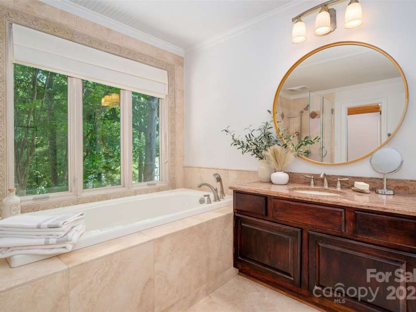 6259 River Cabin Lane, Charlotte, NC 28278.  MLS# CAR4271955, YatesRealty ID 22576. Luxurious primary bathroom showcasing a travertine soaking tub, walk-in travertine shower, travertine flooring and vanity—all with serene water views.