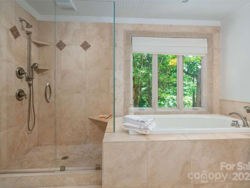 6259 River Cabin Lane, Charlotte, NC 28278.  MLS# CAR4271955, YatesRealty ID 22576. Luxurious primary bathroom showcasing a travertine soaking tub, walk-in travertine shower, travertine flooring and vanity—all with serene water views.