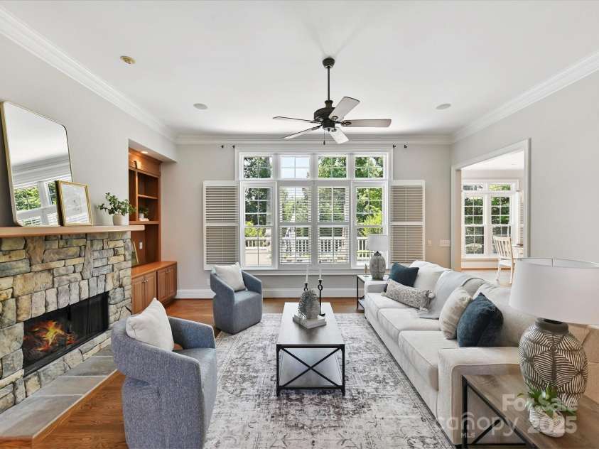 18618 Rollingdale Lane, Davidson, NC 28036.  MLS# CAR4274632, YatesRealty ID 23573. Family room features a stone fireplace flanked by custom built-in wood cabinetry, crown molding, hardwood floors, plantation shutters, and ceiling-mounted speakers beneath a central ceiling fan.