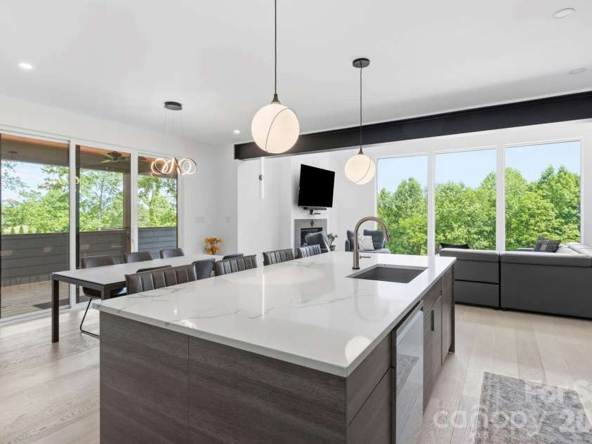 22 Lara Drive, Mills River, NC 28759.  MLS# CAR4382358, YatesRealty ID 23687. Open-concept kitchen and dining space with oversized quartz island, designer lighting, and floor-to-ceiling windows framing lush greenery.