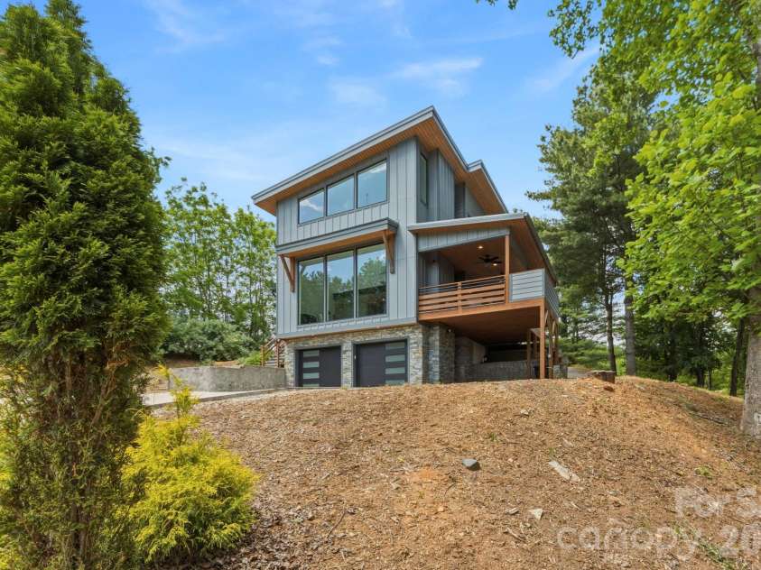 22 Lara Drive, Mills River, NC 28759.  MLS# CAR4382358, YatesRealty ID 23687. Side exterior angle highlighting the elevated covered deck, modern siding, and wooded lot. Designed to maximize both natural light and scenic views.
