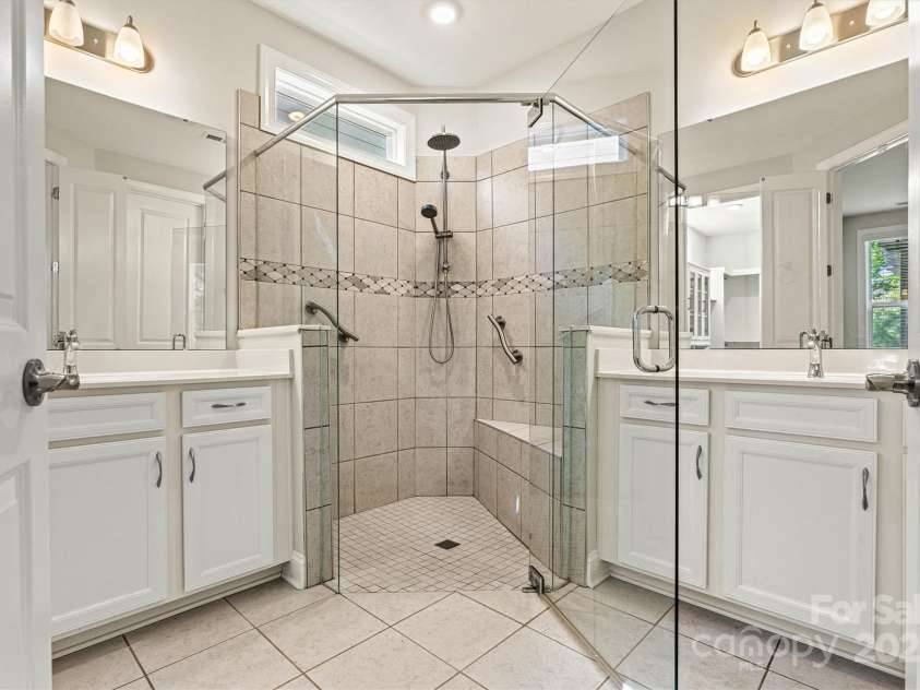 7315 Surprise Court, Charlotte, NC 28215.  MLS# CAR4276101, YatesRealty ID 23823. This spa-like bath features double vanities and a beautifully tiled walk-in shower with corner seat, accent tile, handheld shower, and grab bars—all enhanced by a transom window that lets in soft natural light.