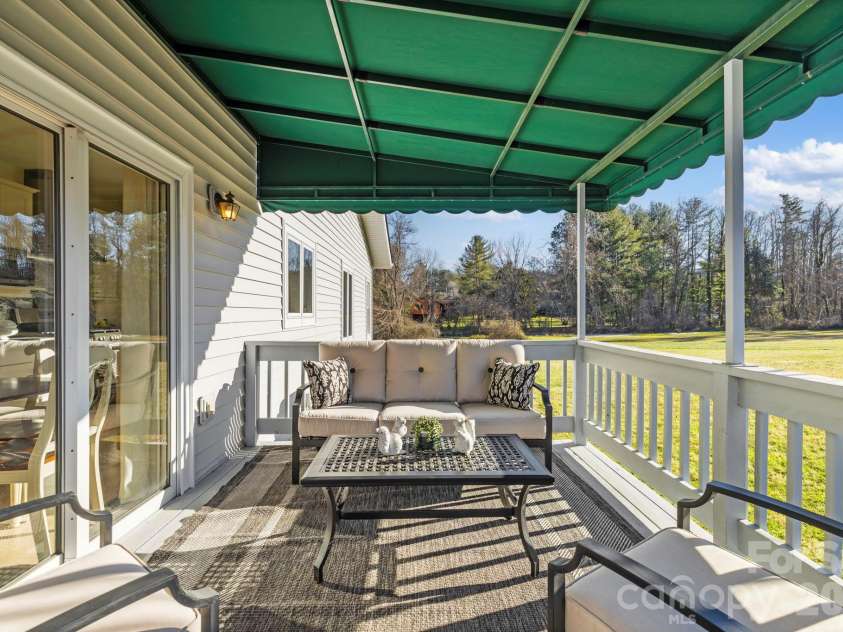 24 Country Meadows Lane, Hendersonville, NC 28792.  MLS# CAR4336584, YatesRealty ID 2420. Covered side porch with outdoor seating, railing, and awning, offering a comfortable spot to enjoy outdoor views