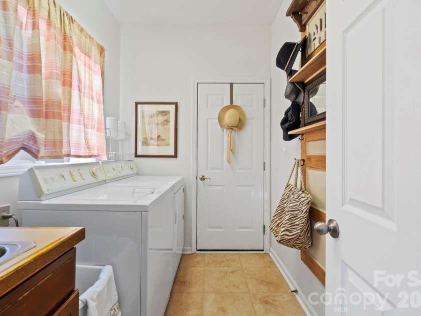 24 Country Meadows Lane, Hendersonville, NC 28792.  MLS# CAR4336584, YatesRealty ID 2420. Functional laundry room with washer and dryer, utility sink, tile flooring, and wall-mounted storage for everyday convenience