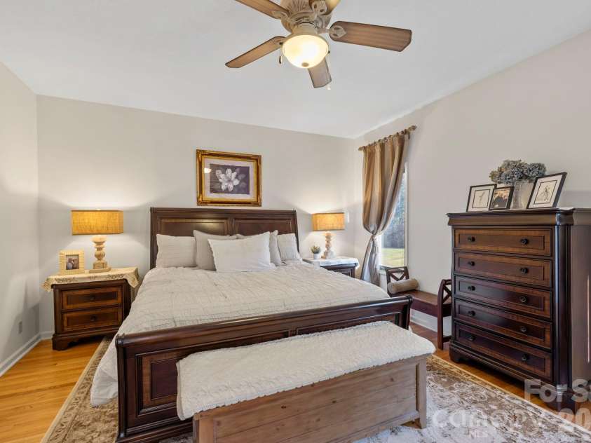 24 Country Meadows Lane, Hendersonville, NC 28792.  MLS# CAR4336584, YatesRealty ID 2420. Spacious primary bedroom with hardwood floors, ceiling fan, large windows, and a calm neutral palette for comfortable everyday living