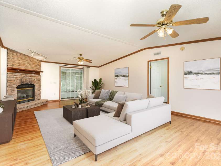 611 Robinson Street, Dallas, NC 28034.  MLS# CAR4261429, YatesRealty ID 24747. Virtually staged.  Cozy living room with wood burning fireplace - door is to primary bedroom.  This home features a split bedroom plan - primary on one end of the home and 2 secondary bedrooms on the other.