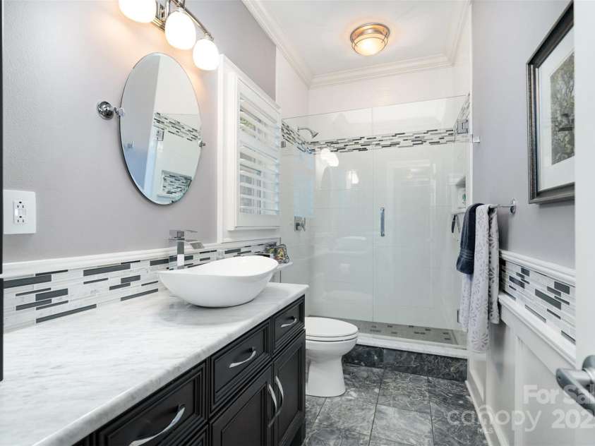 3813 Beauvista Drive, Charlotte, NC 28269.  MLS# CAR4275235, YatesRealty ID 25268. Secondary bath with marble floors, wainscotting. The above counter cabinet has clear glass front doors for linens