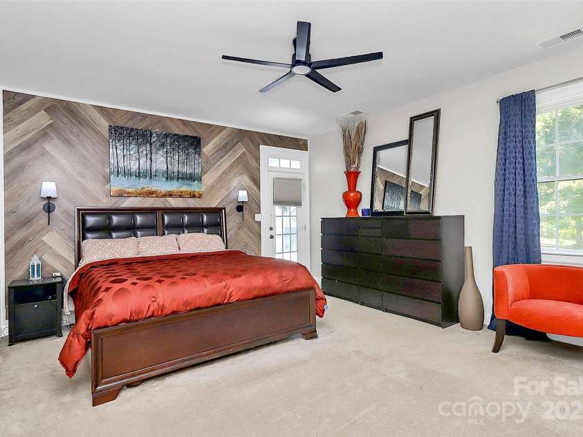 514 Bethel School Road, Clover, SC 29710.  MLS# CAR4278192, YatesRealty ID 25320. Spacious primary bedroom with wood accent wall and entry from the tiered deck complete with hot tub and string lights.