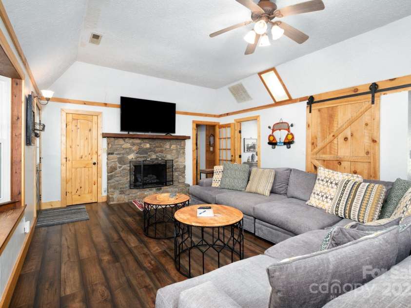 104 Riddle Cove Road, Maggie Valley, NC 28751.  MLS# CAR4257628, YatesRealty ID 25771. Inviting living room with stone fireplace, barn door accents, and access to bedroom wing.