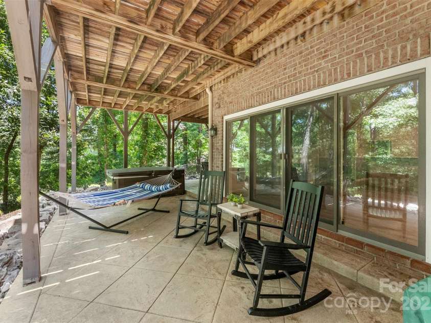 10007 Hillspring Drive, Huntersville, NC 28078.  MLS# CAR4272682, YatesRealty ID 25864. The covered lower level features stamped concrete, a charming brick fireplace, and an 8-person hot tub—all overlooking a private, fenced backyard