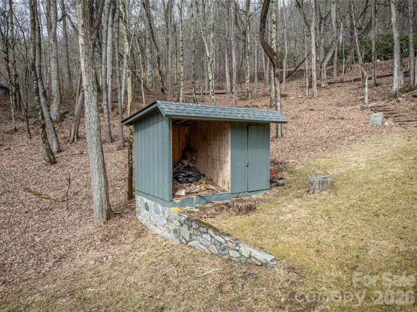 453 Friendly Acres Drive, Waynesville, NC 28786.  MLS# CAR4351574, YatesRealty ID 2664. Stone-based accessory structure offering convenient outdoor storage, blending seamlessly with the natural wooded setting.