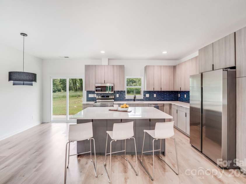 6907 Lancaster Highway, Waxhaw, NC 28173.  MLS# CAR4247480, YatesRealty ID 26742. Anchored by a spacious center island topped with gleaming quartz countertops, the kitchen features sleek custom cabinetry, including floor-to-ceiling pantry cabinets and extra storage beneath the breakfast bar — blendi