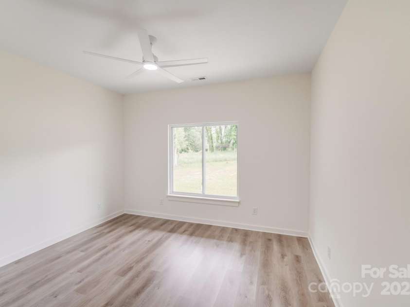 6907 Lancaster Highway, Waxhaw, NC 28173.  MLS# CAR4247480, YatesRealty ID 26742. Located off a private hallway to the left of the kitchen, the secondary bedroom offers backyard views and features a sleek modern white ceiling fan and the same beautiful natural wood-look luxury vinyl plank flooring. 