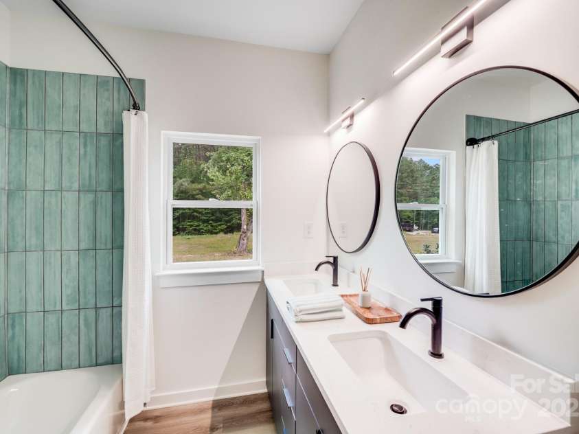 6907 Lancaster Highway, Waxhaw, NC 28173.  MLS# CAR4247480, YatesRealty ID 26742. The full bath features double undermount sinks with quartz countertops, matte black faucets, black-framed circular mirrors, and sleek modern lighting. The tub-shower combination is accented by a vibrant custom green ti