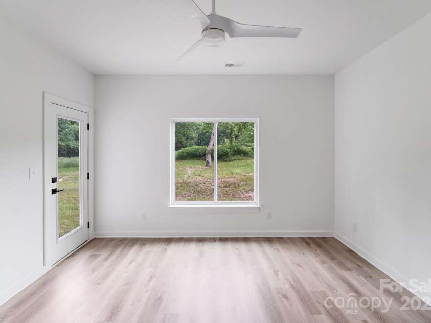 6907 Lancaster Highway, Waxhaw, NC 28173.  MLS# CAR4247480, YatesRealty ID 26742. The primary bedroom features a private door leading to the covered back patio, beautiful natural wood-look luxury vinyl plank flooring, and a large double window overlooking the spacious, tree-lined backyard — creating