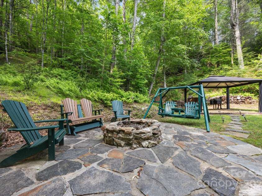 305 Pound Mill Branch Road, Green Mountain, NC 28740.  MLS# CAR4268058, YatesRealty ID 26814. Stone seating area and in-ground firepit. Stairs off to the side lead down to the stream.