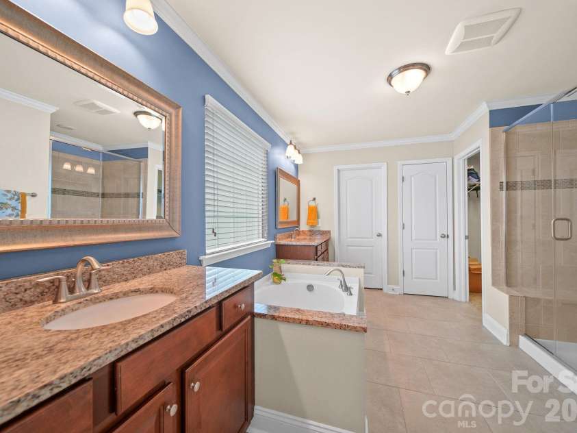 148 Byers Commons Drive, Mooresville, NC 28117.  MLS# CAR4368080, YatesRealty ID 27301. Owner's suite bath featuring dual vanities separated by a garden tub, a glass walk in tiled shower with built in features, his and hers closets, and a private water closet.