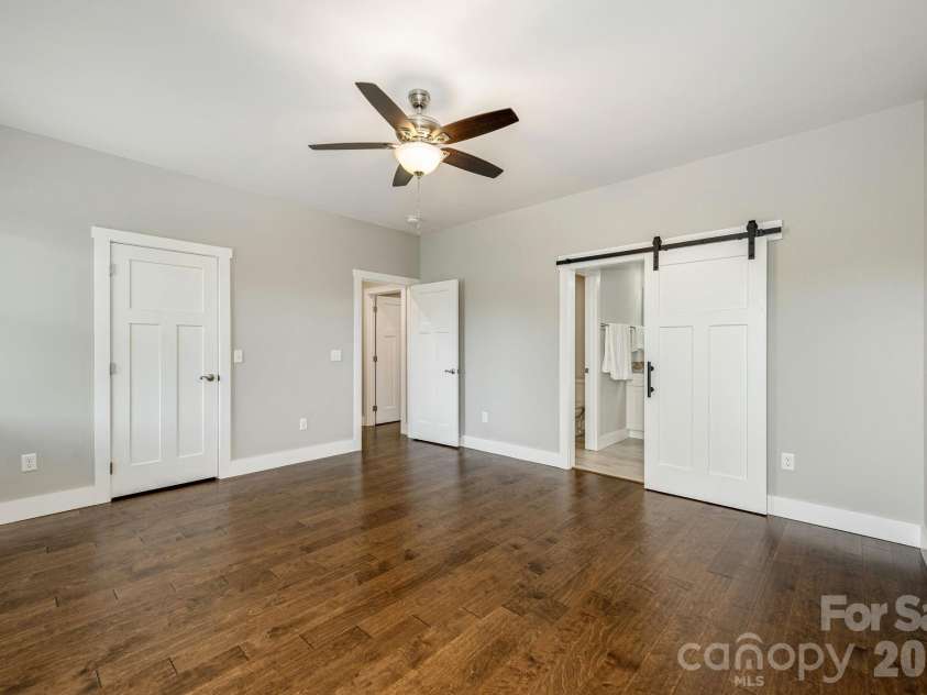 36 Windy Acres Knoll Drive, Hendersonville, NC 28792.  MLS# CAR4377336, YatesRealty ID 27383. Primary Bedroom – Generously sized primary suite with engineered wood flooring, ceiling fan, and convenient sliding barn door leading to the private en-suite bath.