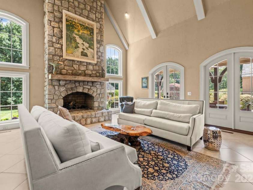343 Wester Brewlands Road, Iron Station, NC 28080.  MLS# CAR4284507, YatesRealty ID 28060. The stunning two-story great room features a soaring stone fireplace, vaulted ceilings with exposed beams, and an abundance of natural light from arched French doors and oversized windows—offering both warmth 