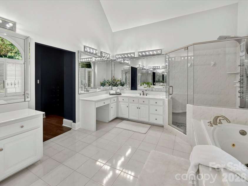 4725 Old Course Drive, Charlotte, NC 28277.  MLS# CAR4384171, YatesRealty ID 28405. The spa-inspired primary bath features dual vanities, a soaking tub beneath an elegant arched window, a spacious glass-enclosed walk-in shower, and soaring vaulted ceilings for a luxurious retreat.