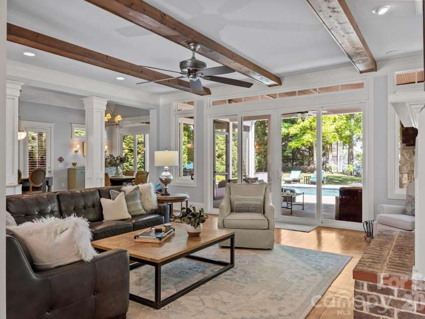 20727 Pointe Regatta Drive, Cornelius, NC 28031.  MLS# CAR4370865, YatesRealty ID 28632. Light-filled living area with exposed ceiling beams, fireplace, and large sliding doors opening to a covered patio and pool.