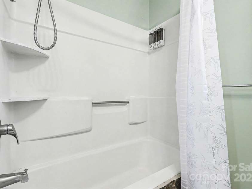 119 Moore Drive, Gastonia, NC 28056.  MLS# CAR4332115, YatesRealty ID 2865. A tub/shower combination with window provides natural light and ventilation, while neutral finishes create a clean, functional space. Wall shelving offers additional storage, making this bathroom both practical and comfortab