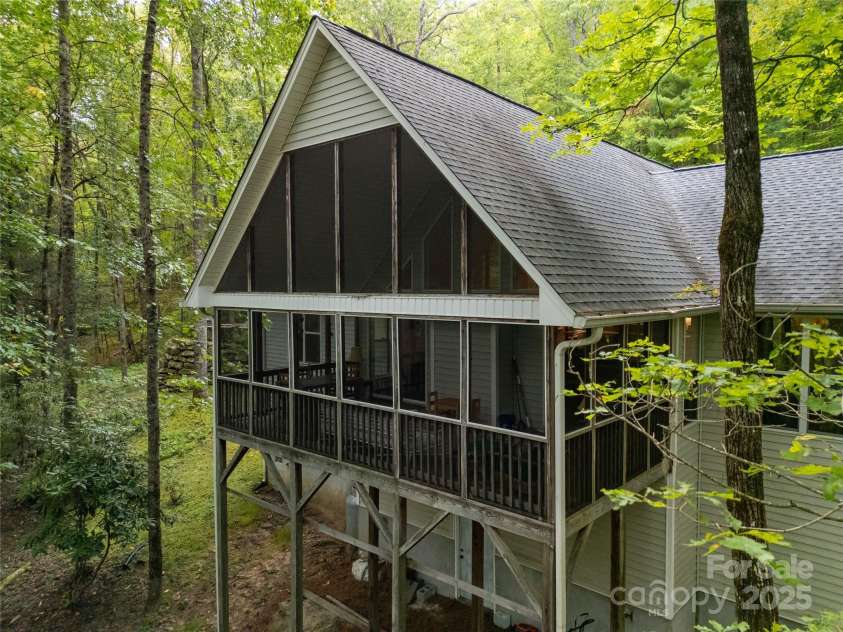 557 Country Club Estates Drive, Sapphire, NC 28774.  MLS# CAR4302980, YatesRealty ID 2977. Rear of the house seen from the air up in the trees looking in at the rear deck / porch. Door to the large crawlspace is visible below.