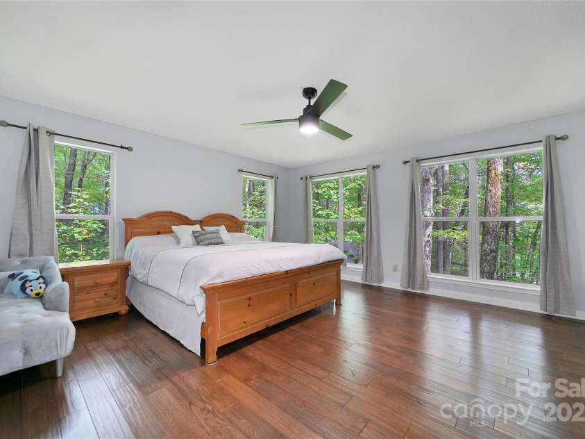 557 Country Club Estates Drive, Sapphire, NC 28774.  MLS# CAR4302980, YatesRealty ID 2977. The primary bedroom has plenty of space and lots of natural light. Watch the birds and squirrels in the tree tops outside! Very private.