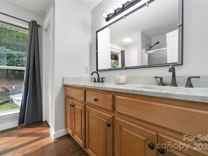 557 Country Club Estates Drive, Sapphire, NC 28774.  MLS# CAR4302980, YatesRealty ID 2977. The primary en-suite bathroom is quite stylish and has a double vanity. Also, large windows looking out to the private front yard and firepit area, if you wish natural light.