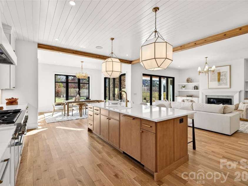 1316 Holmes Drive, Charlotte, NC 28209.  MLS# CAR4338664, YatesRealty ID 3016. View of the open living space from the Kitchen. Gorgeous lighting. Center Island that can accommodate four bar stools. Gas Thermadore stove on left. Looking toward the FP with mantel and bookcases. 