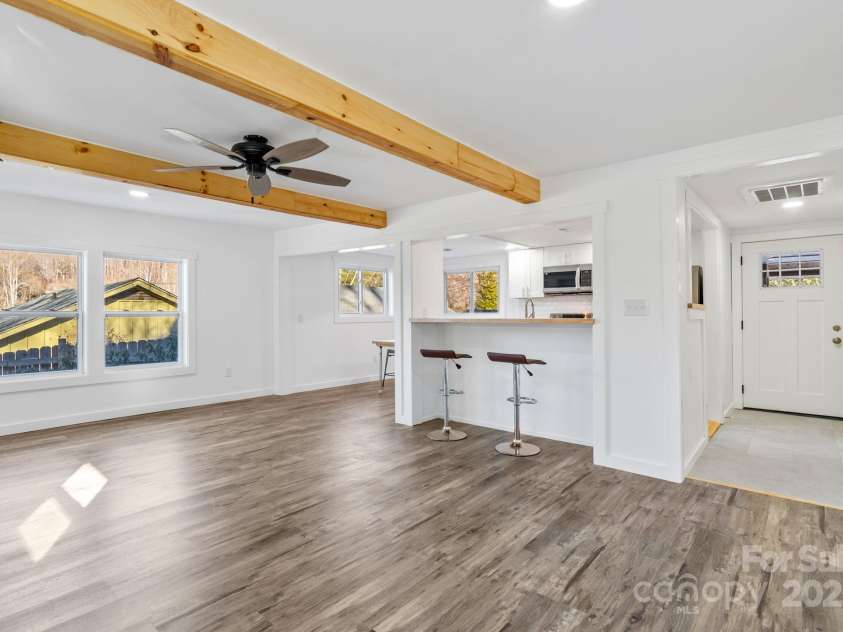 86 Chestnut Hill Road, Gerton, NC 28735.  MLS# CAR4213931, YatesRealty ID 3024. A beautifully renovated living area featuring modern laminate flooring, exposed wooden beams, and a ceiling fan for added comfort. Large windows invite natural light, making the space bright and welcoming, ideal for fami