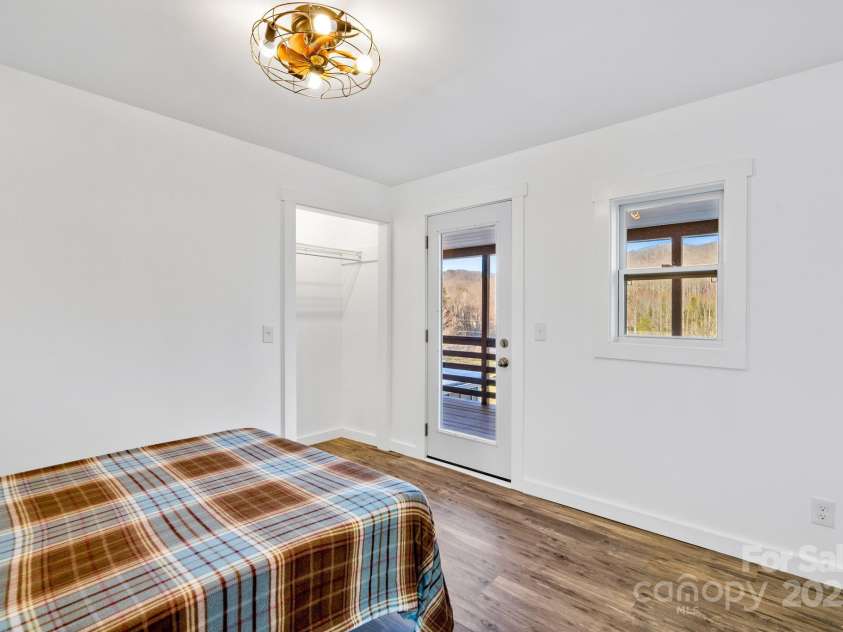 86 Chestnut Hill Road, Gerton, NC 28735.  MLS# CAR4213931, YatesRealty ID 3024. A bright upstairs bedroom (#2) with access to an outdoor balcony, allowing for a seamless indoor-outdoor living experience. The bedroom room features a modern light fixture with fan and laminate flooring for a polished l