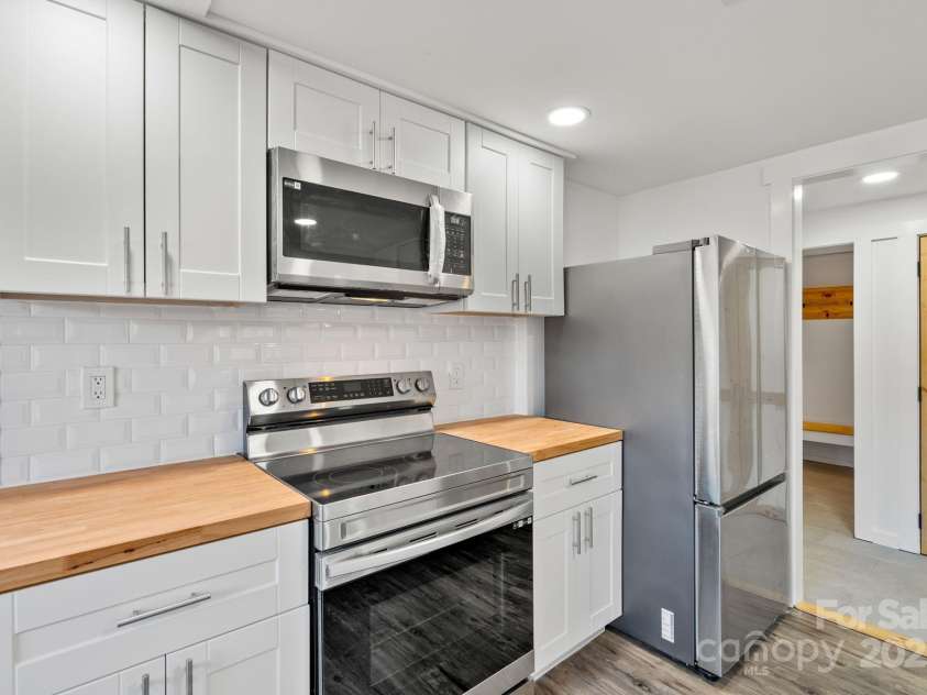 86 Chestnut Hill Road, Gerton, NC 28735.  MLS# CAR4213931, YatesRealty ID 3024. A closer look at the kitchen detailing the clean, minimalist design of the cabinetry, modern hardware, and high-end stainless steel appliances. The tile backsplash and butcher block countertops add warmth and texture to 