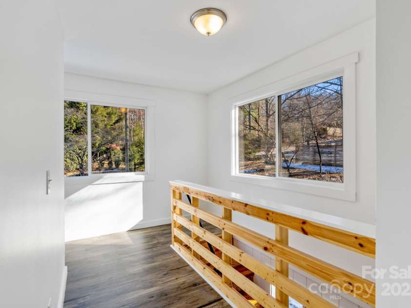 86 Chestnut Hill Road, Gerton, NC 28735.  MLS# CAR4213931, YatesRealty ID 3024. A cozy upper-level landing with large windows offering serene views of the surrounding landscape. The natural wood railings and light-filled space make this area a peaceful retreat within the home.