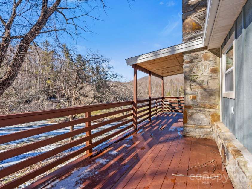 86 Chestnut Hill Road, Gerton, NC 28735.  MLS# CAR4213931, YatesRealty ID 3024. A spacious side deck with a mix of covered and open areas, accented by beautiful stonework, lies just off the living room. This area provides an ideal spot for outdoor dining or relaxing while enjoying the natural surrou