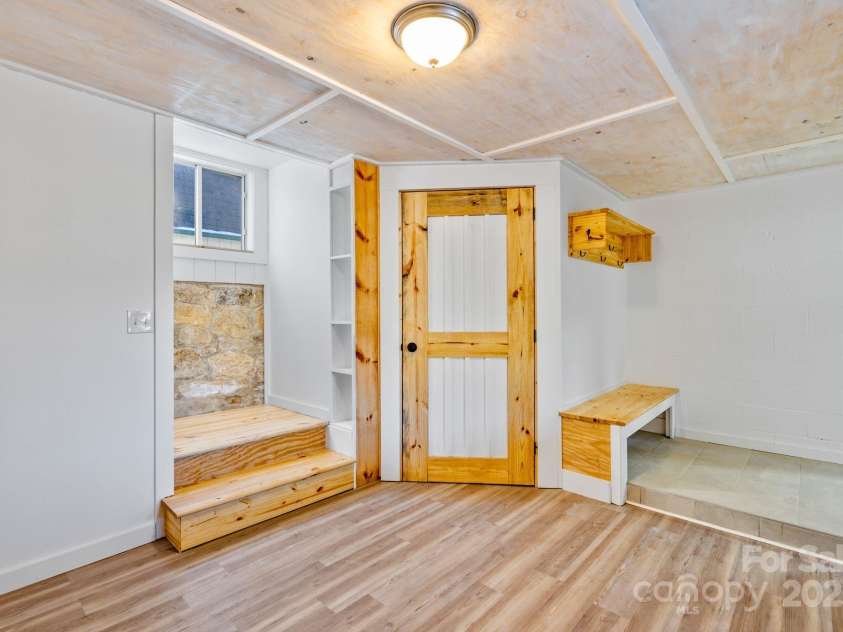 86 Chestnut Hill Road, Gerton, NC 28735.  MLS# CAR4213931, YatesRealty ID 3024. Another angle of the mudroom showcasing its thoughtful design, including a wooden door with rustic charm, open shelving, and tiled flooring for easy maintenance.