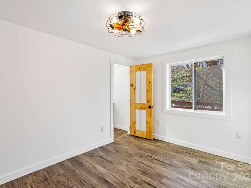 86 Chestnut Hill Road, Gerton, NC 28735.  MLS# CAR4213931, YatesRealty ID 3024. The downstairs bedroom features warm laminate flooring, a unique light fixture with fan, and large windows that provide ample natural light. The wood-accented doors add a touch of rustic elegance to the space, making it 
