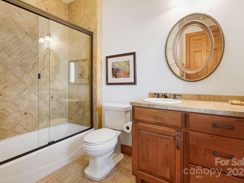 197 Cherry Knob Drive, Mars Hill, NC 28754.  MLS# CAR4271284, YatesRealty ID 30496. Private ensuite bath features a full-size tub and shower with tile surround, warm wood cabinetry, perfect for guest comfort and style.