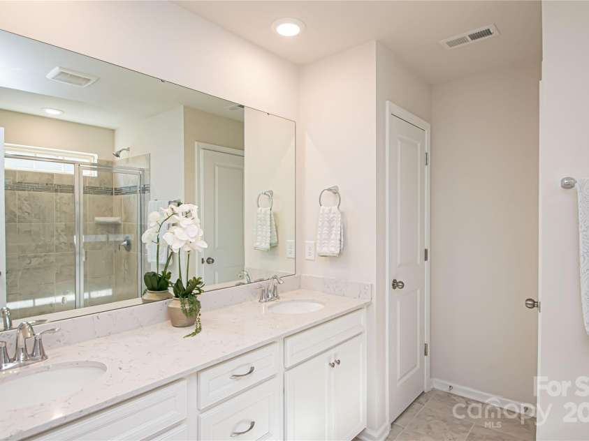 17637 Snug Harbor Road, Charlotte, NC 28278.  MLS# CAR4283392, YatesRealty ID 30990. The primary bathroom features white cabinetry with dual sinks, recessed lighting, tile floor and shower, a linen closet, private water closet, and a spacious walk-in shower with a built-in bench.