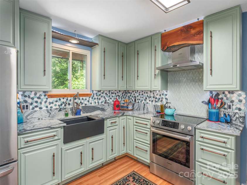 160 Tracy Place, Clyde, NC 28721.  MLS# CAR4282174, YatesRealty ID 31389. Bright and stylish kitchen featuring sage green cabinetry, striking granite countertops, a farmhouse sink, and unique tile backsplash accented by natural wood details.