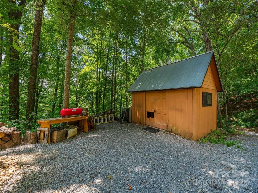 160 Tracy Place, Clyde, NC 28721.  MLS# CAR4282174, YatesRealty ID 31389. Detached storage building with metal roof, surrounded by mature trees and ample gravel parking area.