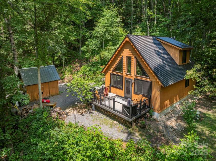 160 Tracy Place, Clyde, NC 28721.  MLS# CAR4282174, YatesRealty ID 31389. Private mountain retreat featuring an A-frame cabin with metal roof, spacious front deck, and detached storage building, all nestled among lush, wooded surroundings.