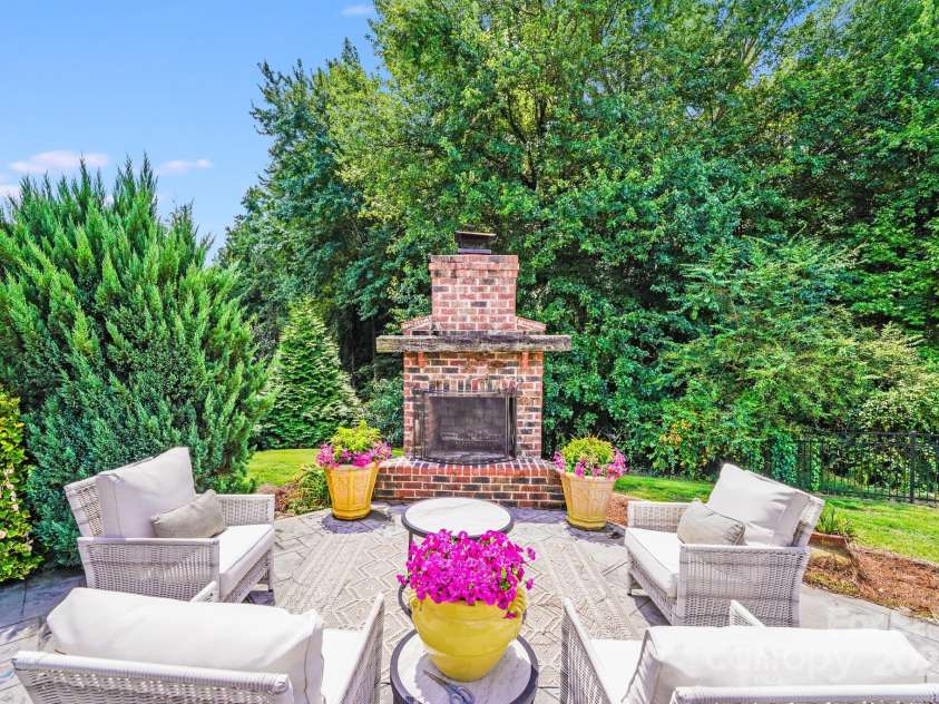 2702 Arsdale Road, Waxhaw, NC 28173.  MLS# CAR4287994, YatesRealty ID 32277. This inviting outdoor living area features a classic brick fireplace surrounded by lush landscaping—perfect for cozy gatherings or peaceful evenings under the stars