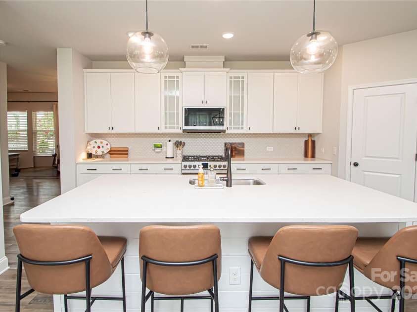 1061 Ansley Park Drive, Fort Mill, SC 29707.  MLS# CAR4281028, YatesRealty ID 32626. The kitchen features a large island, white cabinetry, quartz countertops, tile backsplash, stainless steel appliances, and brushed nickel hardware—perfectly blending style and function.
